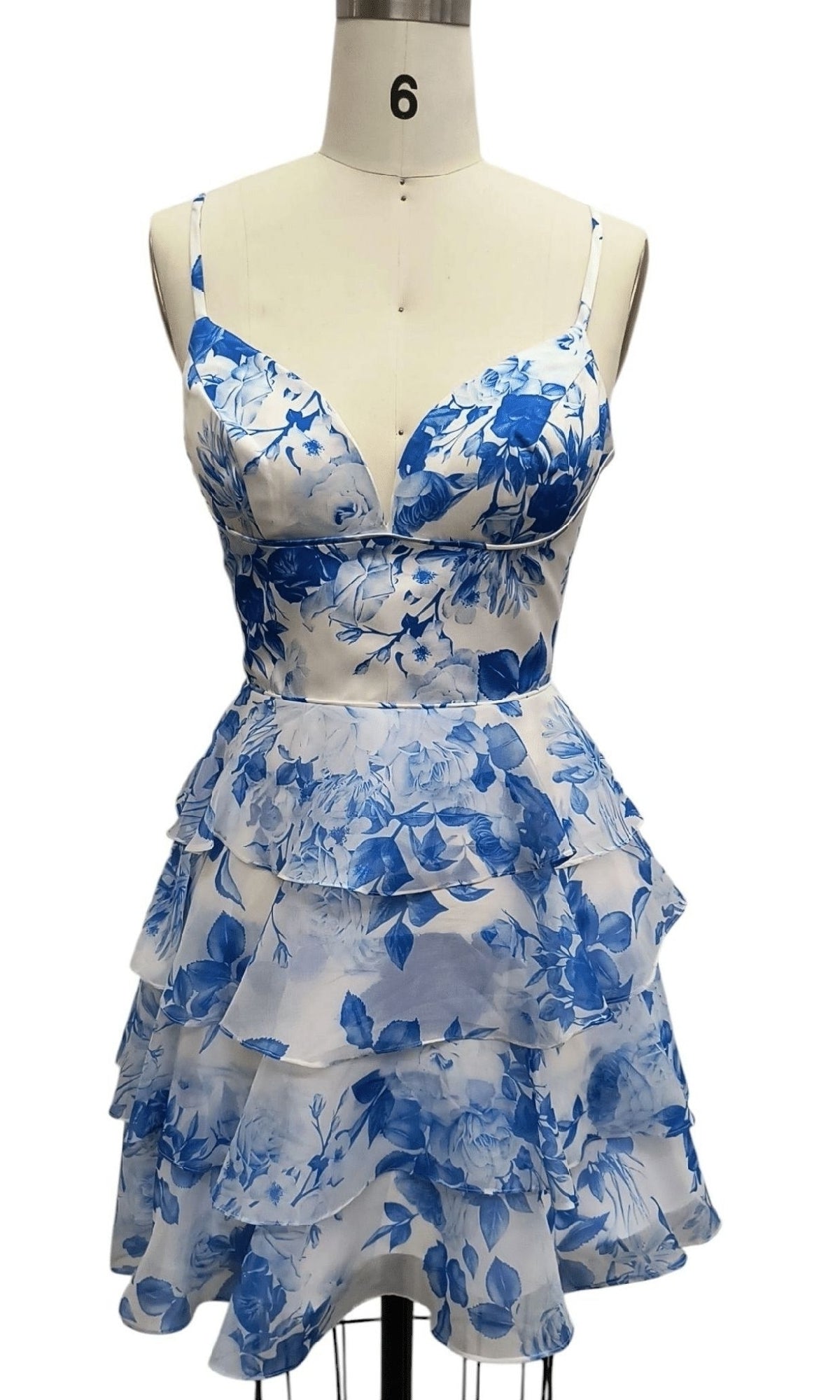 Short Blue Print Hoco Dress: 12612 features a blue and white floral pattern, sleeveless a-line fit, deep V-neckline, fitted bodice, and tiered ruffle skirt, shown on a dress form.